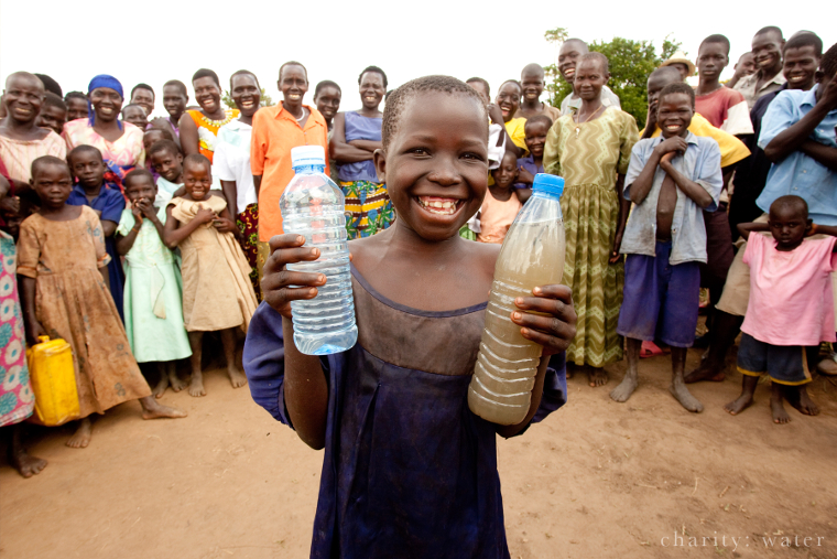 Ugandan holding two bottles: one with dirty water, the other with clean water